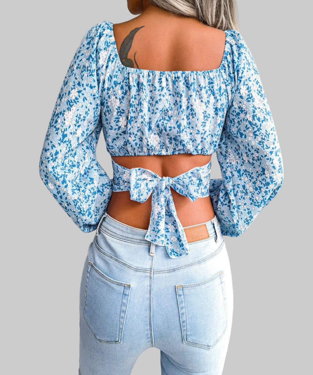 Person wearing a blue floral top with a tie detail and light blue jeans indoors.