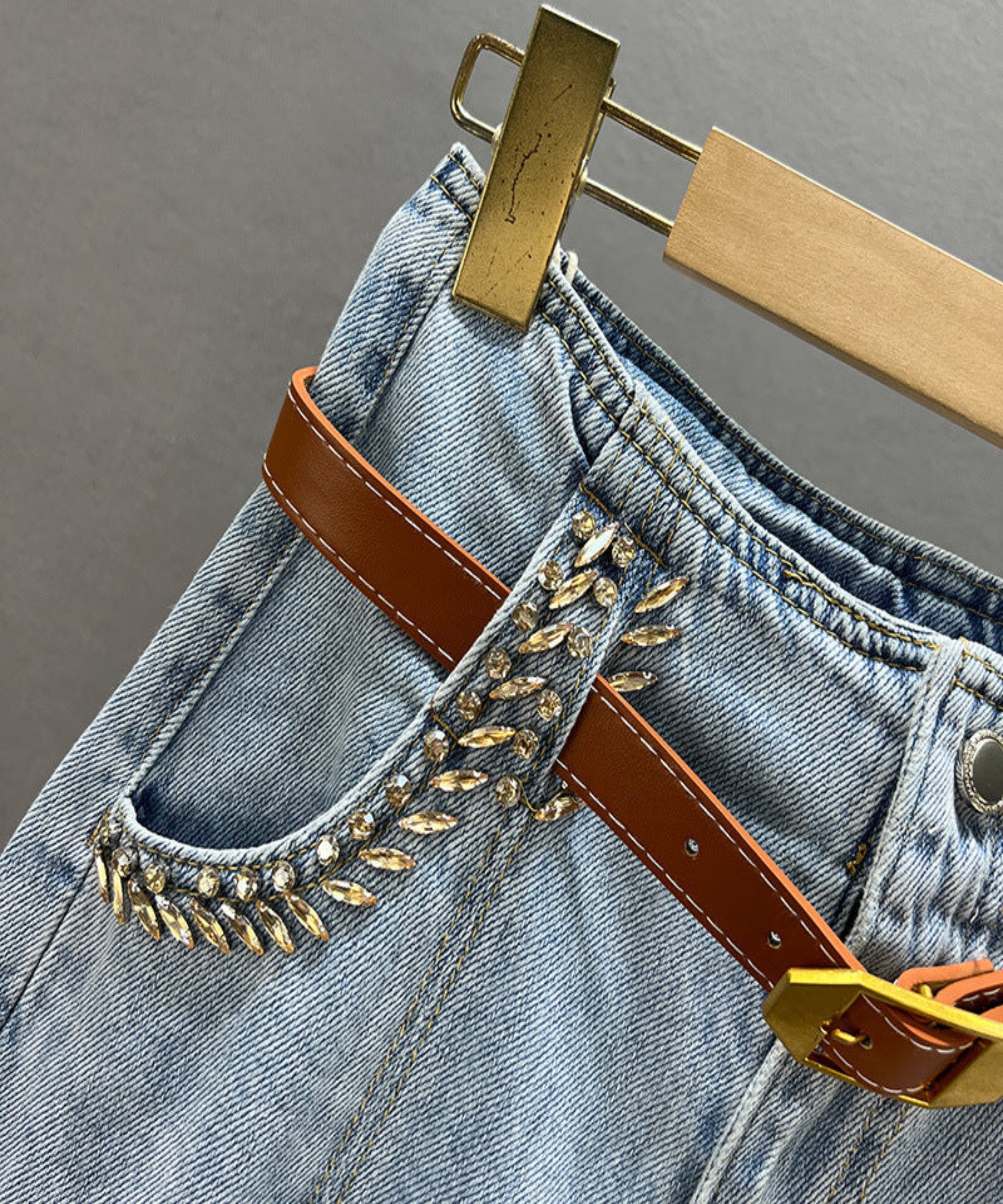 Close-up of blue denim jeans with a brown belt and decorative elements on a gray background