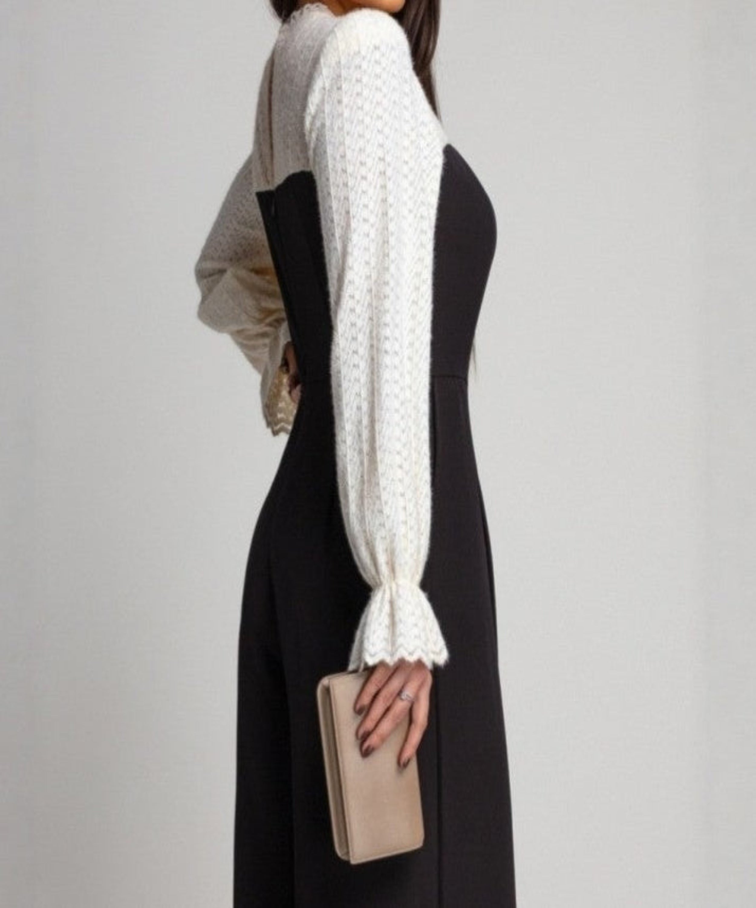 Woman wearing a black dress with a white and gray shawl over her shoulders against a plain background
