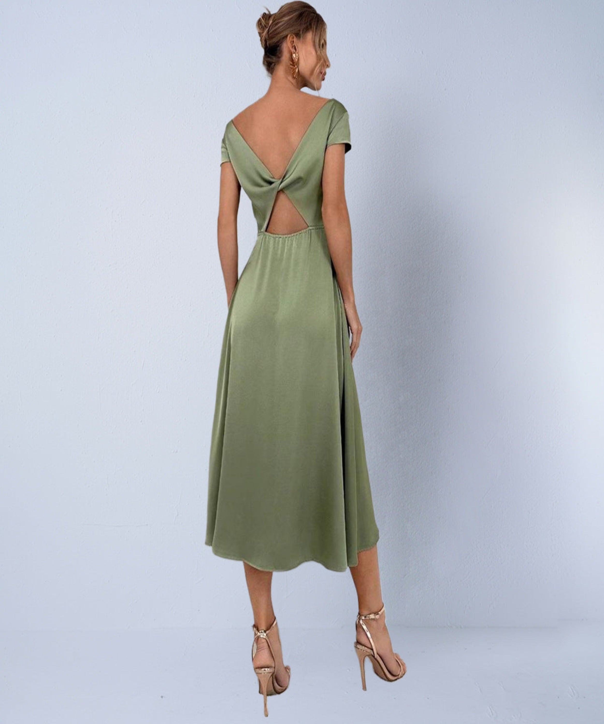 Woman wearing a green dress with cut-out back on a light gray background