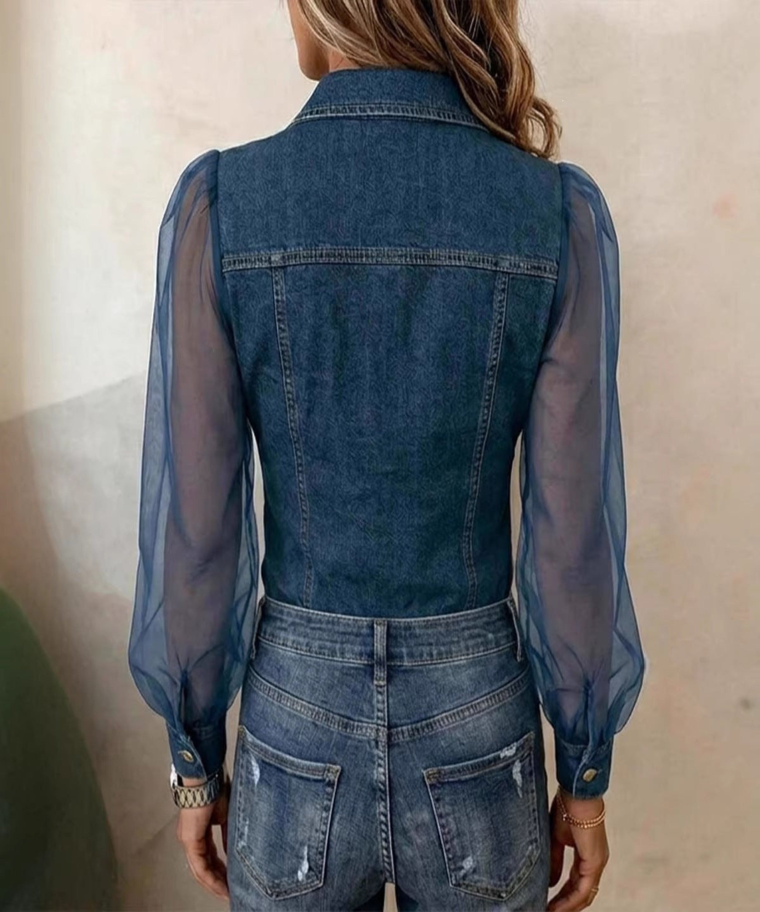 Person wearing a denim outfit with sheer sleeves against a neutral background