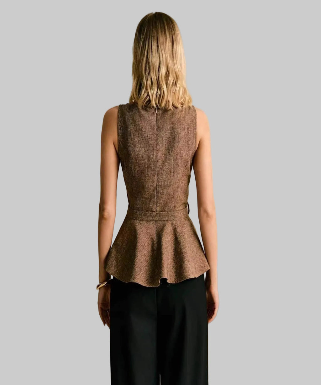 Woman wearing a brown peplum top and black pants against a beige background