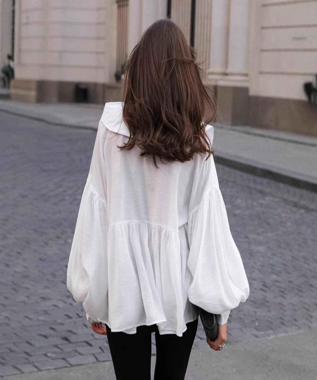 Person wearing a white blouse with sheer panels on a street.