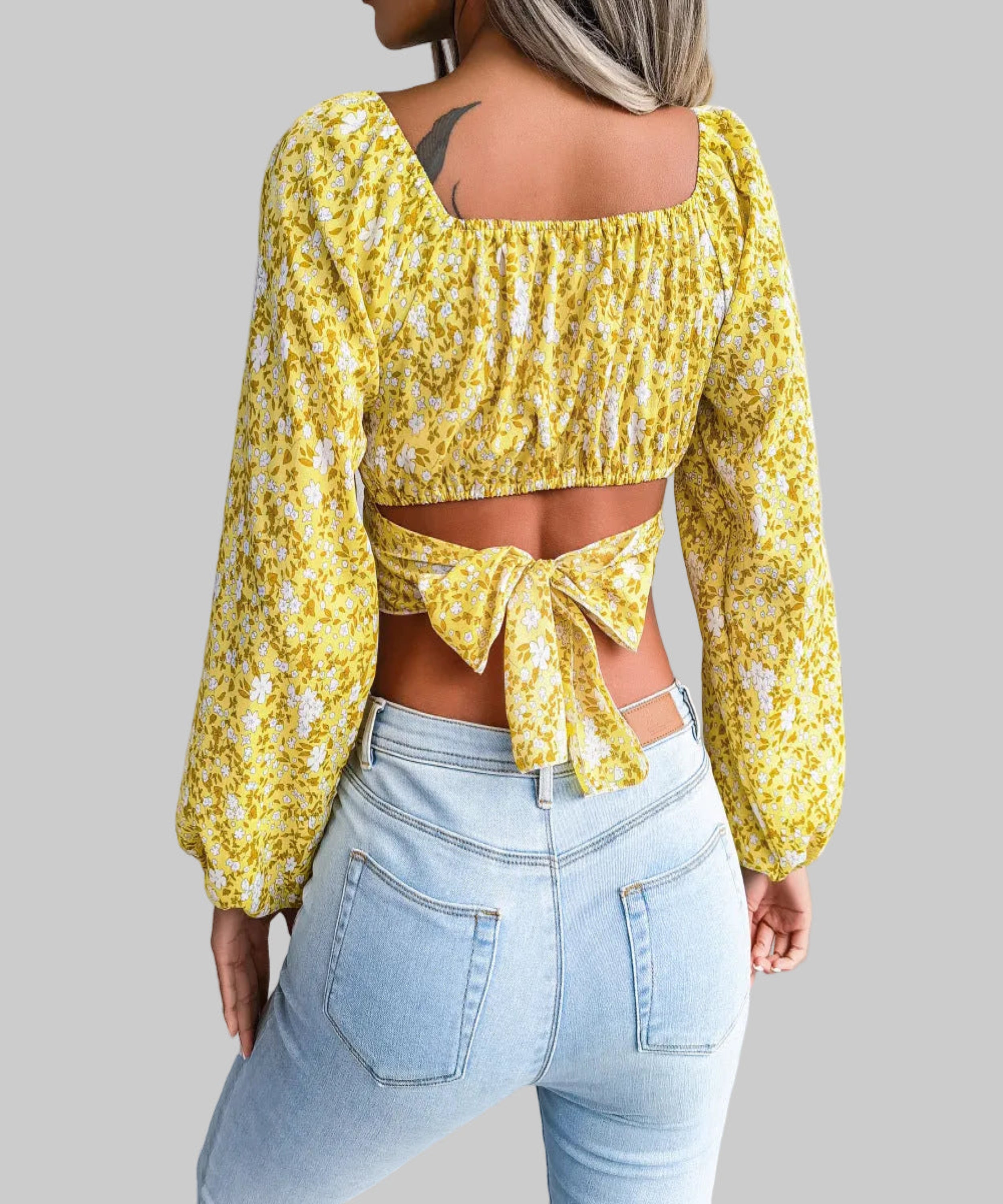 Person wearing a yellow floral top with a tied front and light blue jeans in an indoor setting.