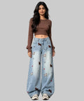 Woman in brown top and light blue jeans with animal prints on  a white background.