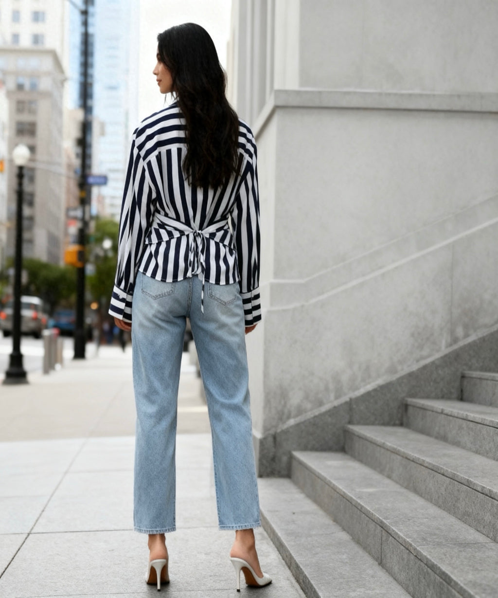 Woman wearing a black and white striped shirt and light blue jeans standing on a city street.