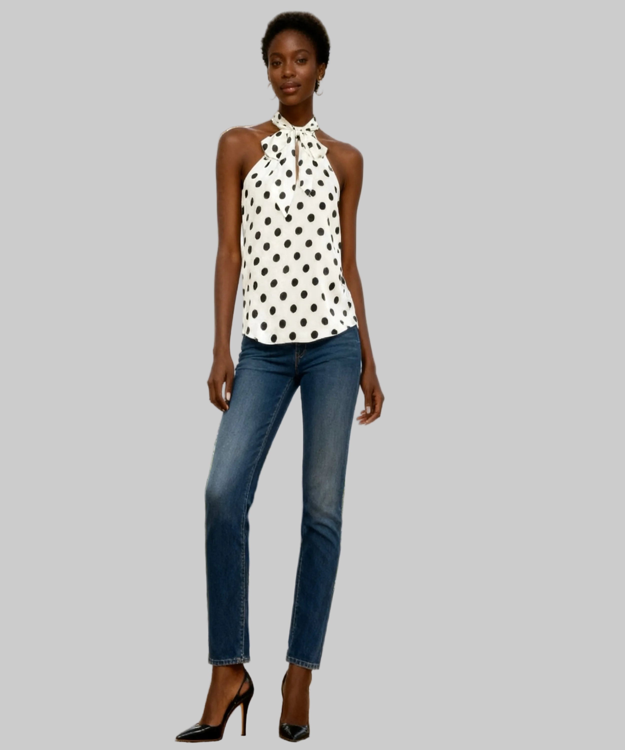 Woman wearing a polka dot top and jeans standing in a white background.