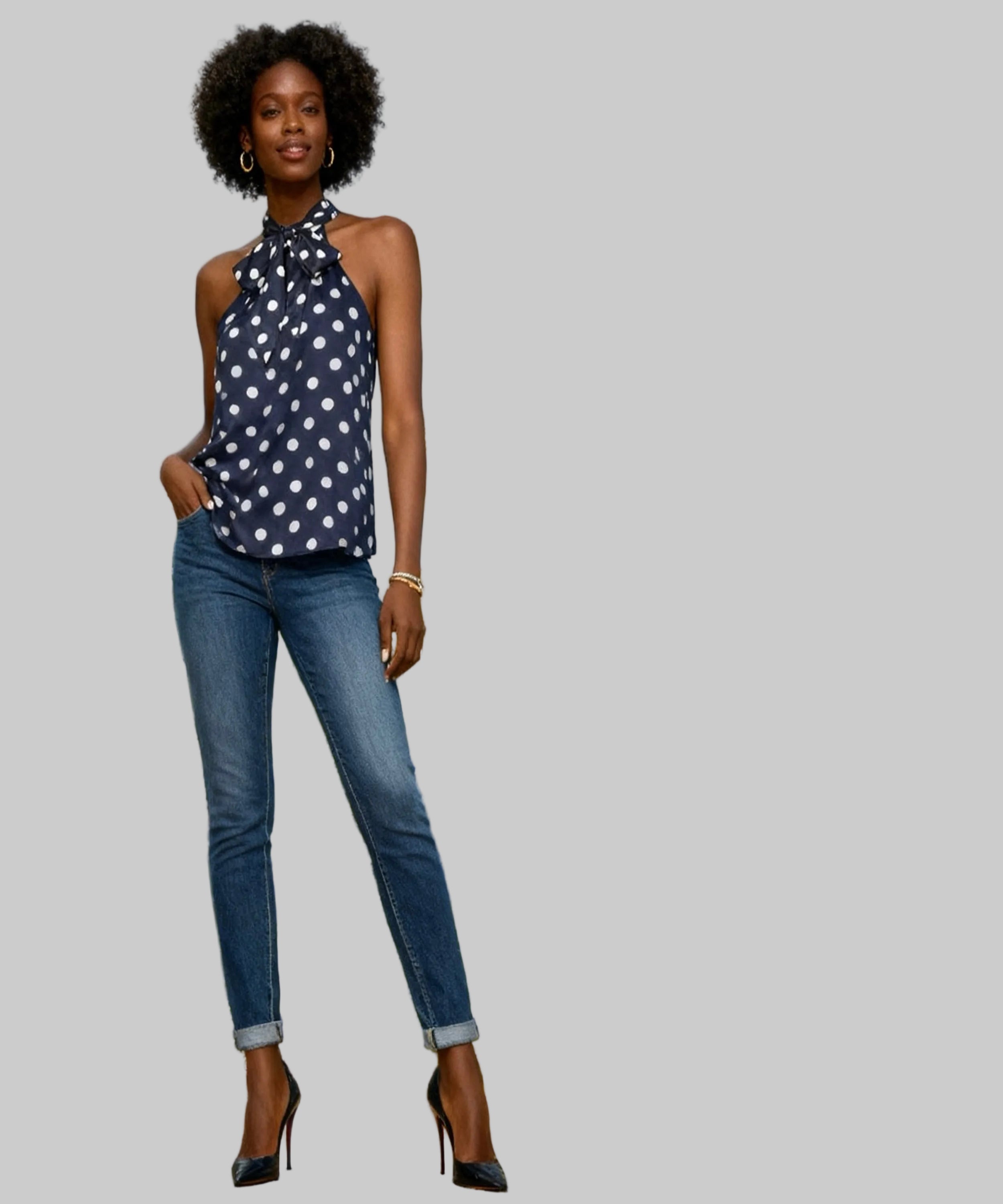 Woman in a polka dot top and jeans standing in a white background.