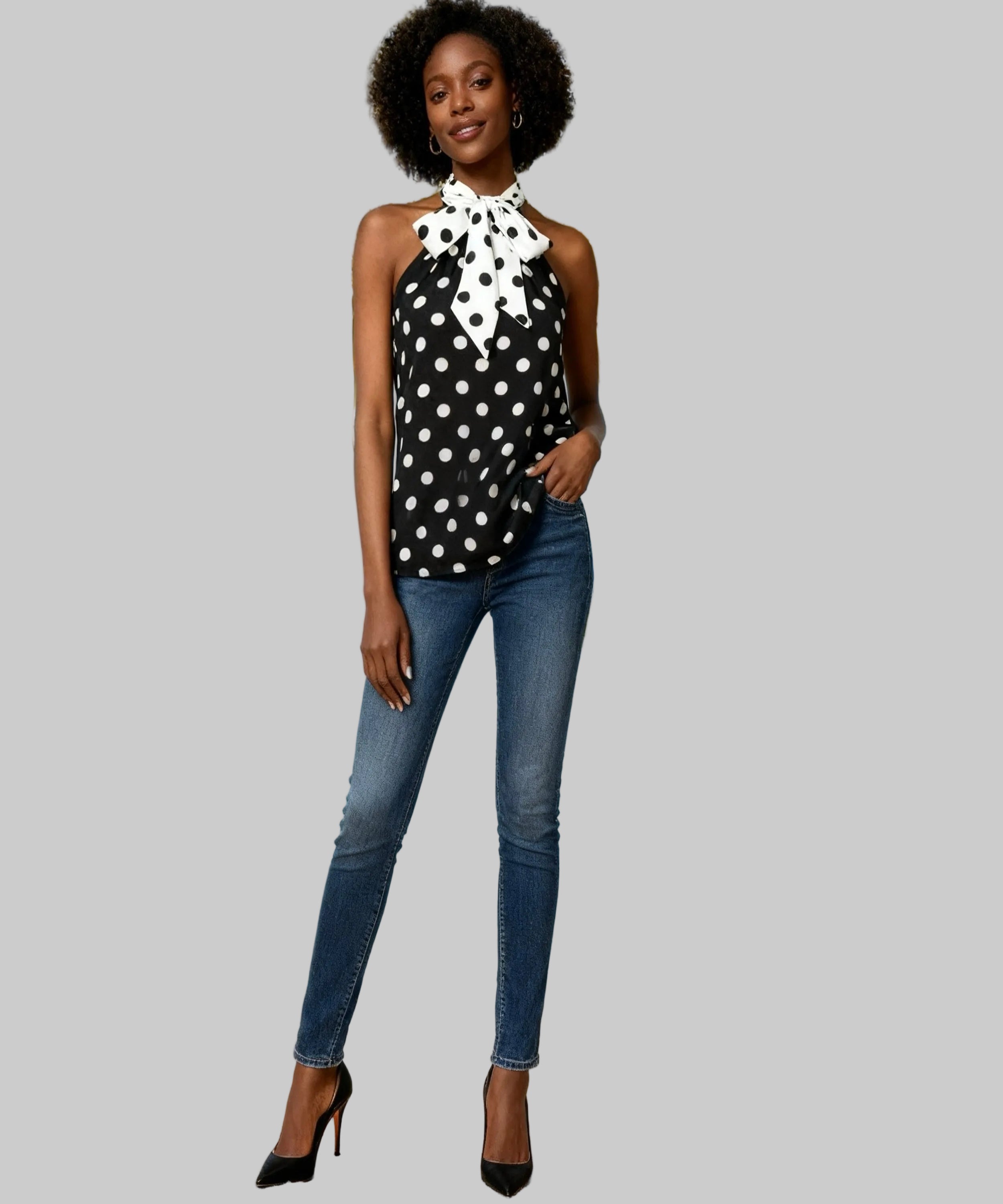 Woman in polka dot top and jeans standing on white background.
