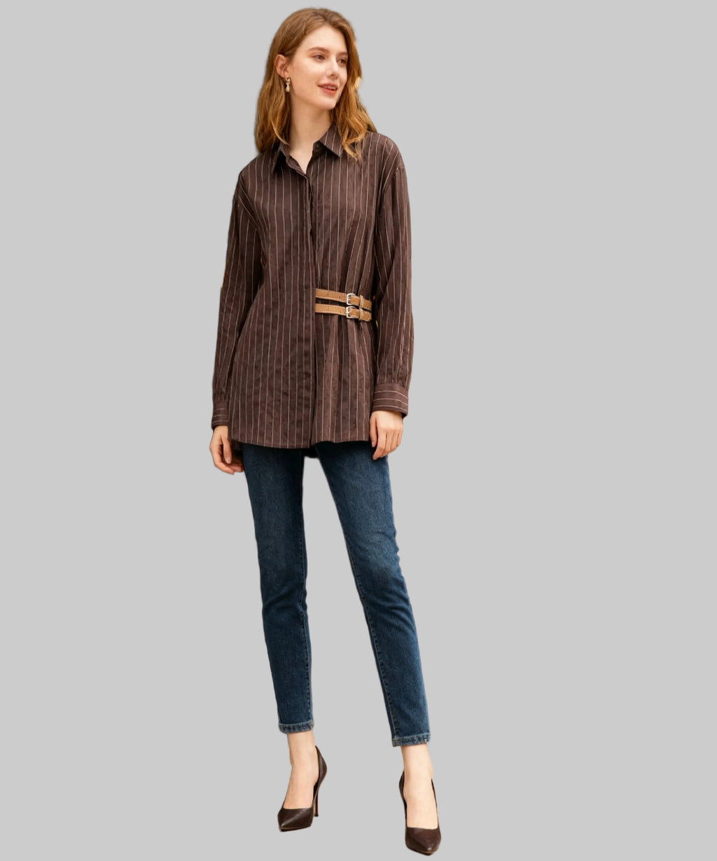 Woman standing in a white background wearing a brown striped shirt and blue jeans.