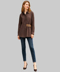 Woman standing in a white background wearing a brown striped shirt and blue jeans.