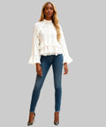 Woman wearing a white blouse with ruffled details and blue jeans in a white background