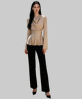 Woman in a beige peplum top and black pants standing on a white background.