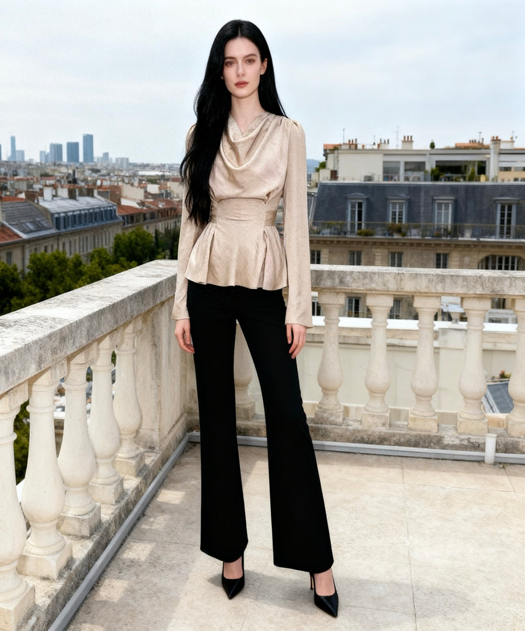 Woman in a beige top and black pants standing on a balcony with a cityscape in the background
