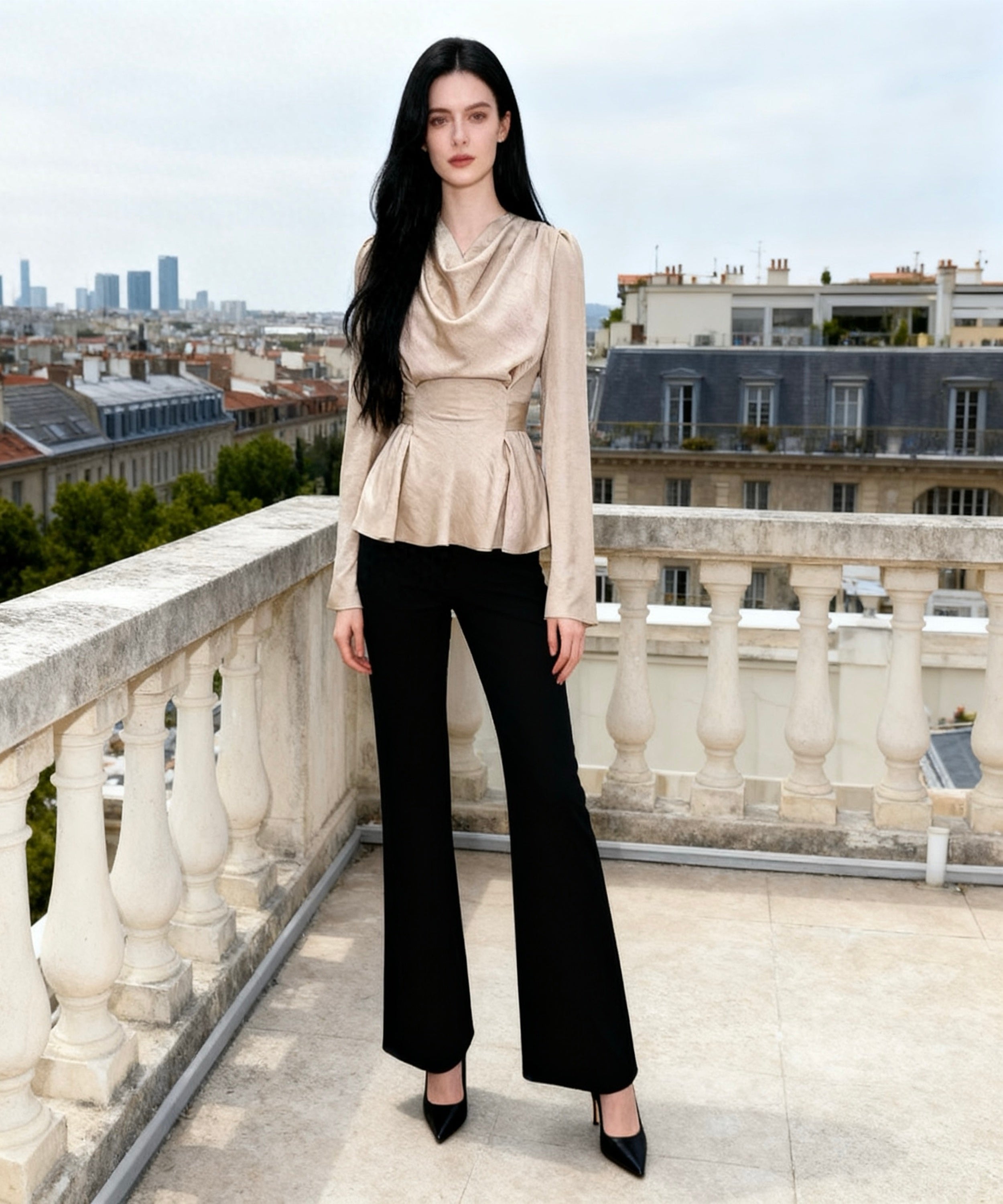 Woman in a beige top and black pants standing on a balcony with a cityscape in the background