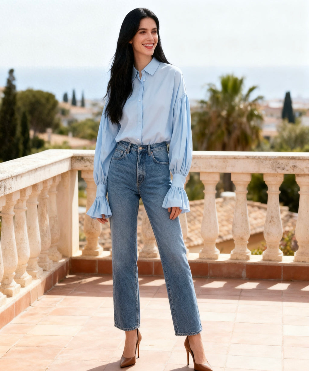 Woman wearing a light blue shirt and jeans standing on a balcony with a scenic background.