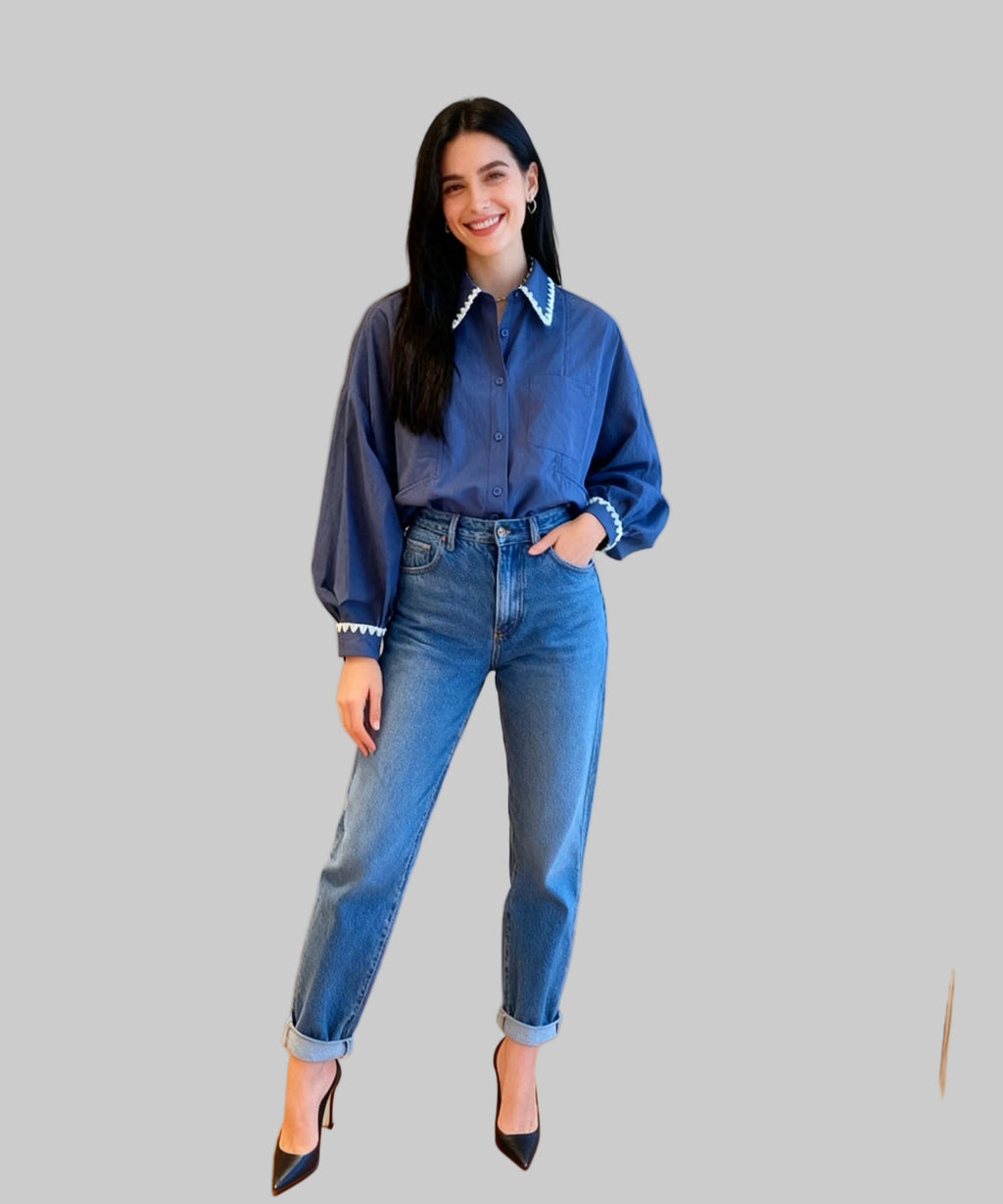 Woman wearing a blue denim shirt and jeans standing on a white background.