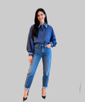 Woman wearing a blue denim shirt and jeans standing on a white background.