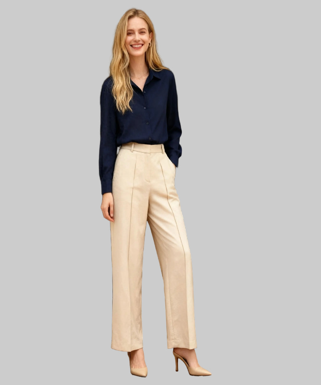 Woman wearing a navy shirt and beige pants standing in a white background.
