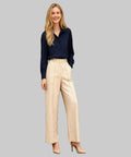 Woman wearing a navy shirt and beige pants standing in a white background.