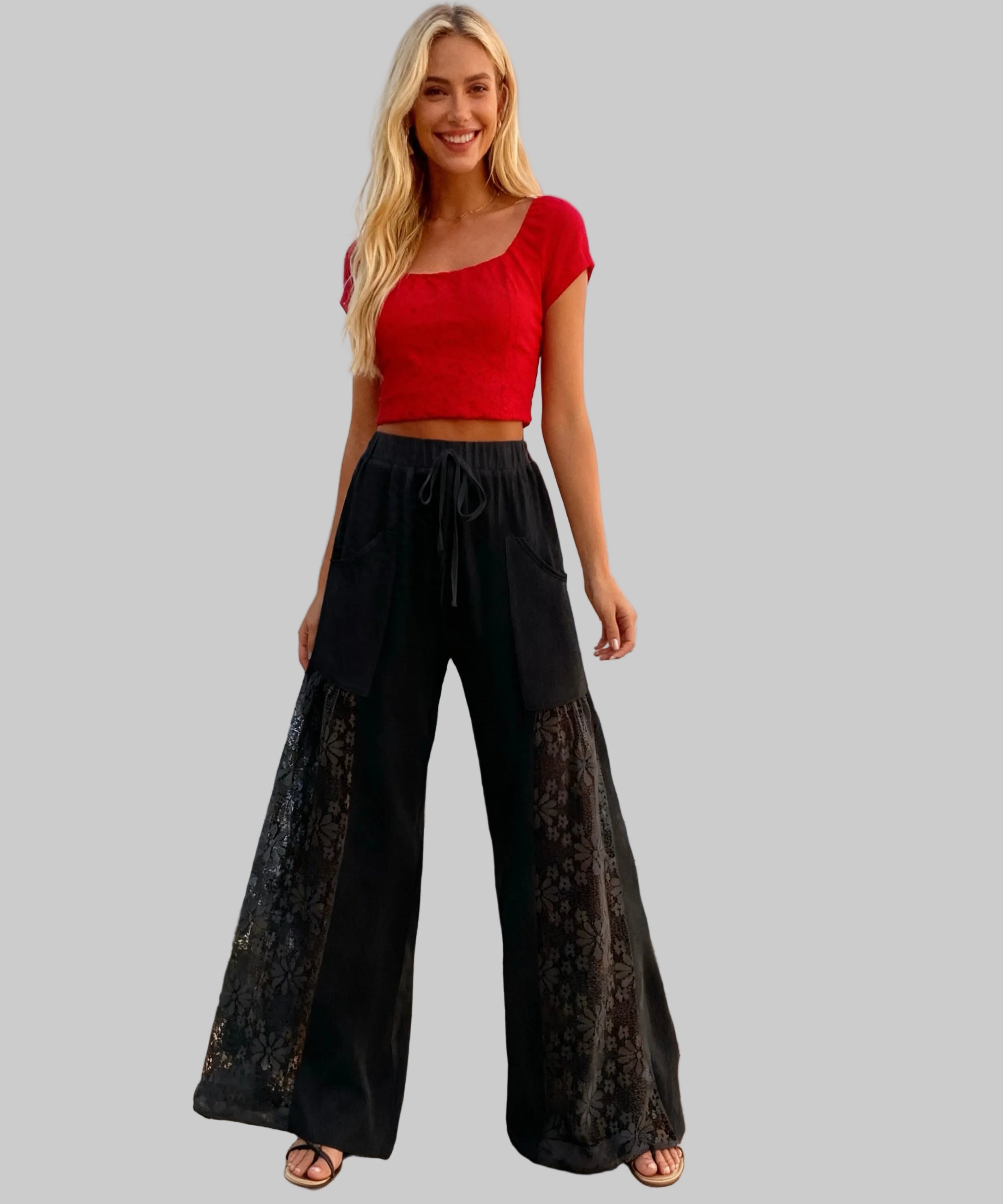 Woman wearing a red top and black lace pants standing on a white background.