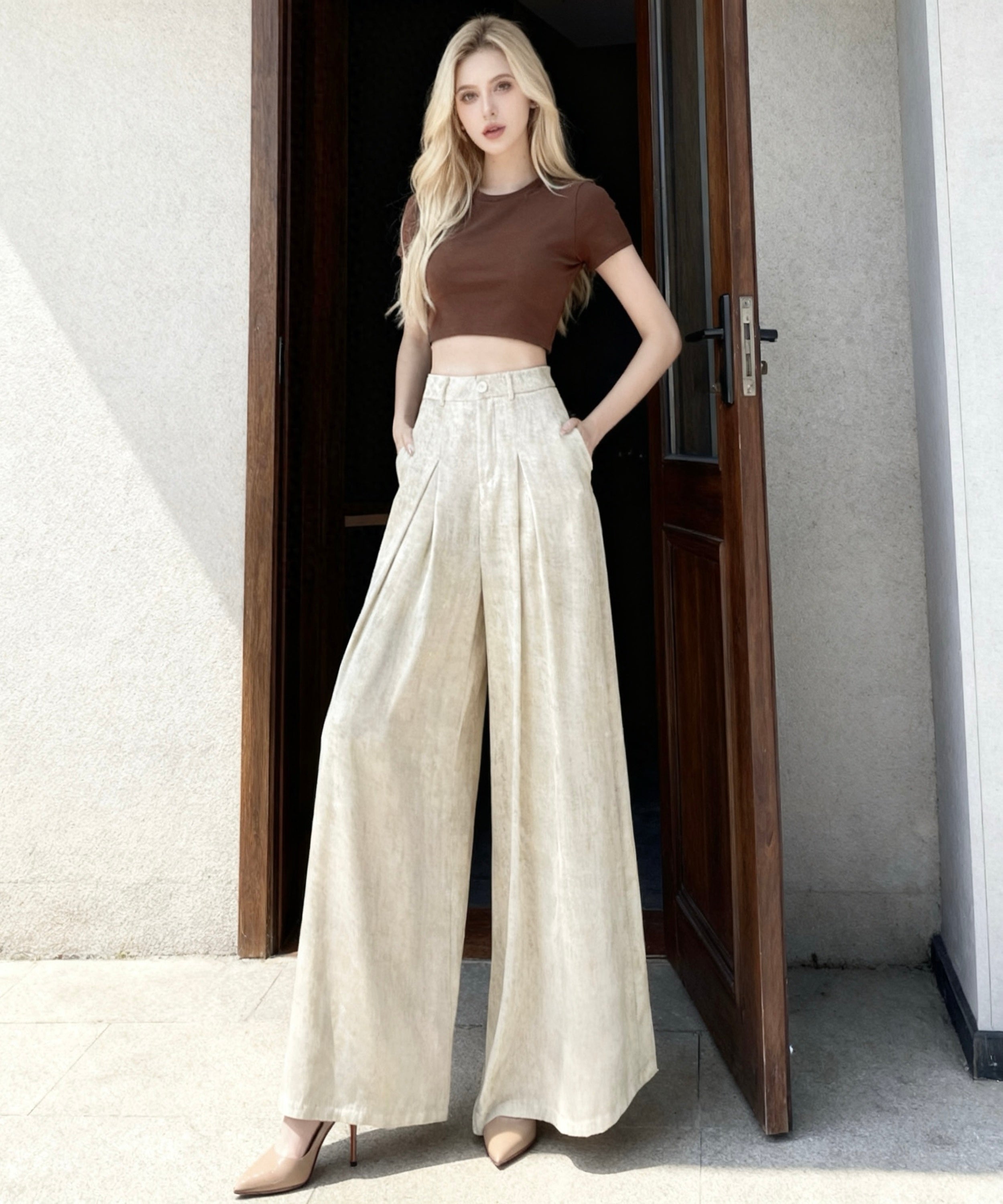 Woman wearing a brown top and white wide-leg pants standing in a doorway.