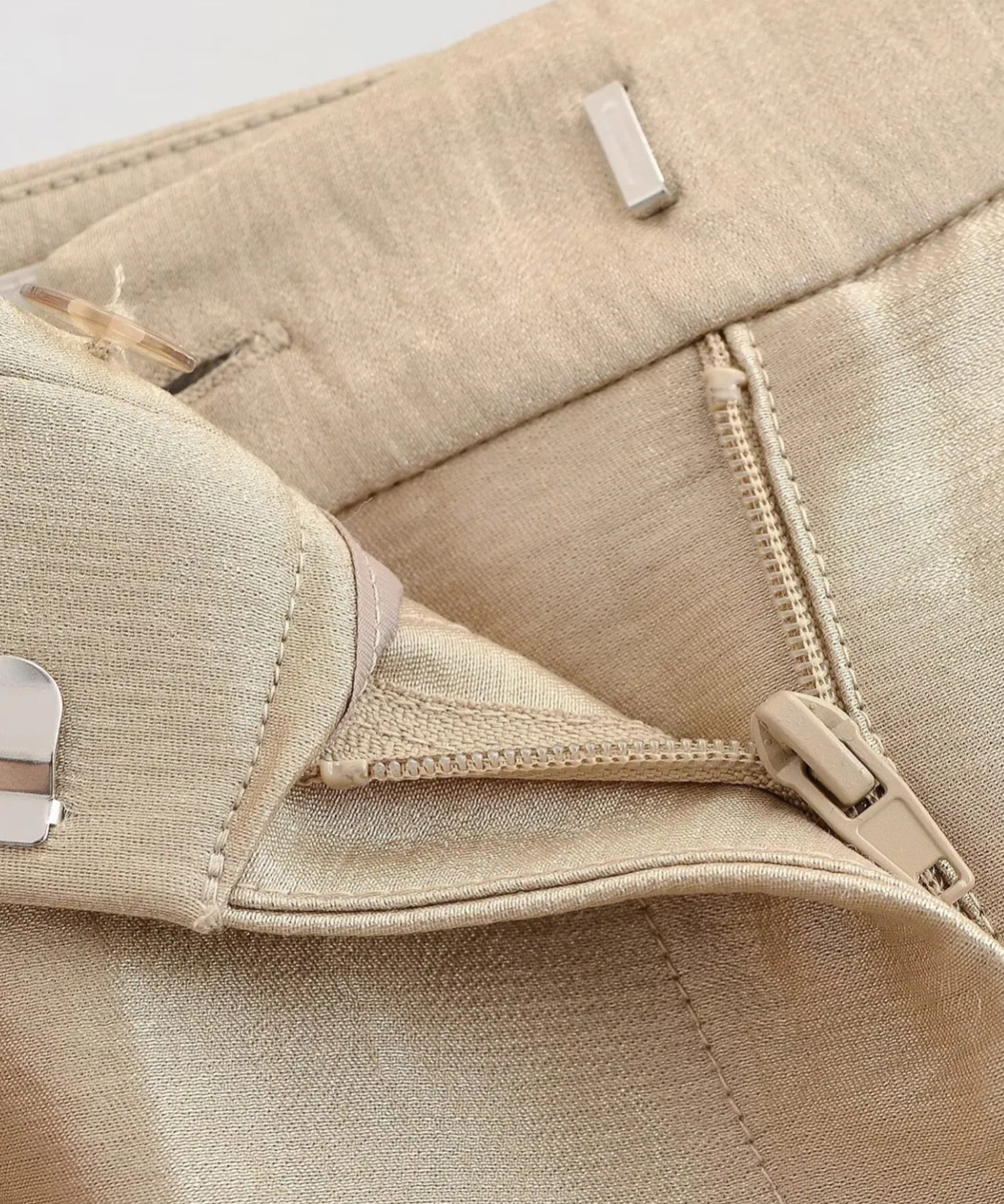 Close-up of a beige fabric bag with zippers and buttons on a light gray background