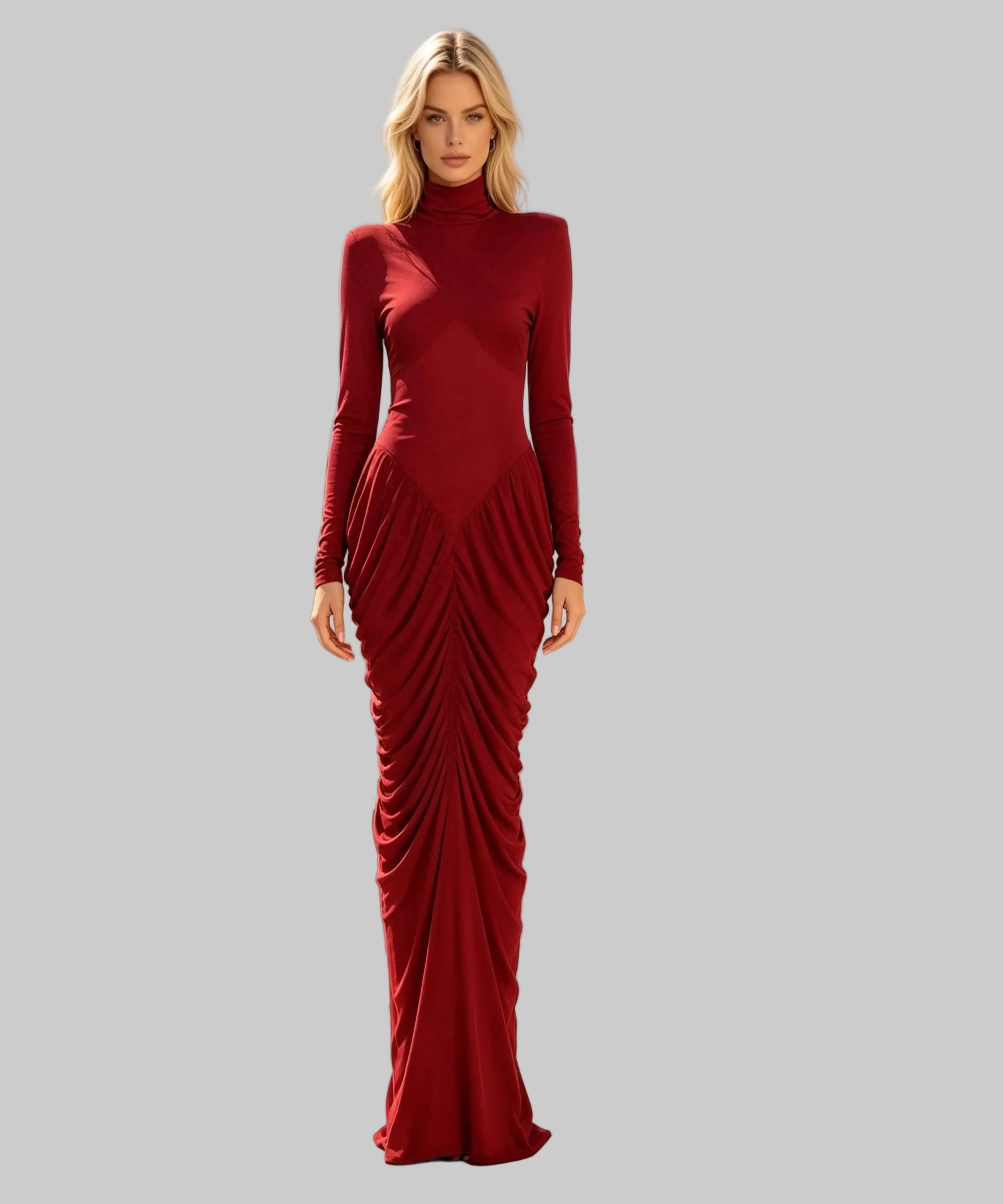 A woman stands on a white background wearing a floor-length, long-sleeve red dress with a high mock neck and dramatic gathered draping at the skirt. 