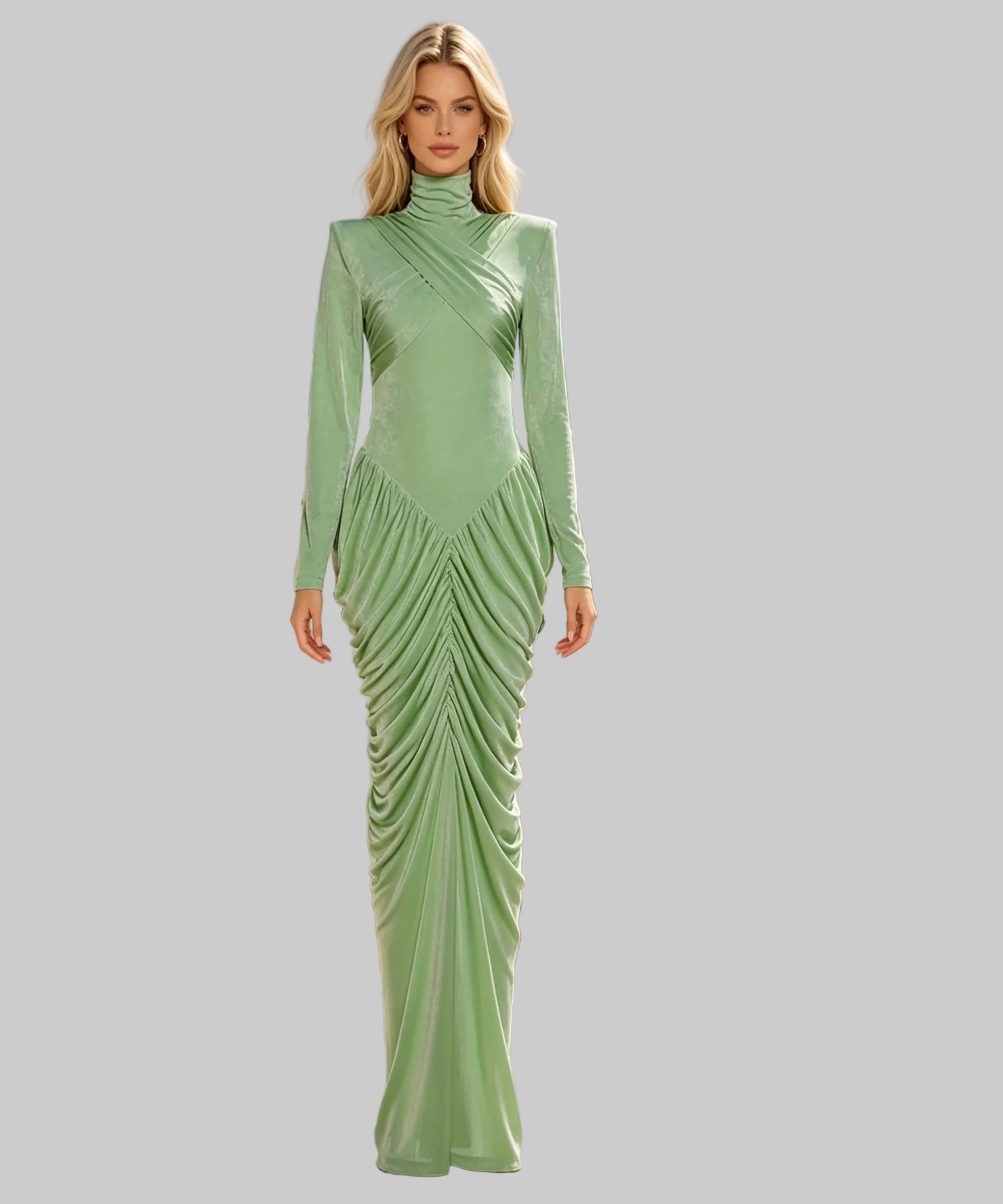 A woman stands on a sunlit terrace wearing a floor-length sage green dress with long sleeves, a high mock neck, and dramatic draped ruching across the bodice and skirt. The background is white