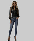 Woman wearing a sheer black top over a denim shirt with blue jeans against a white background