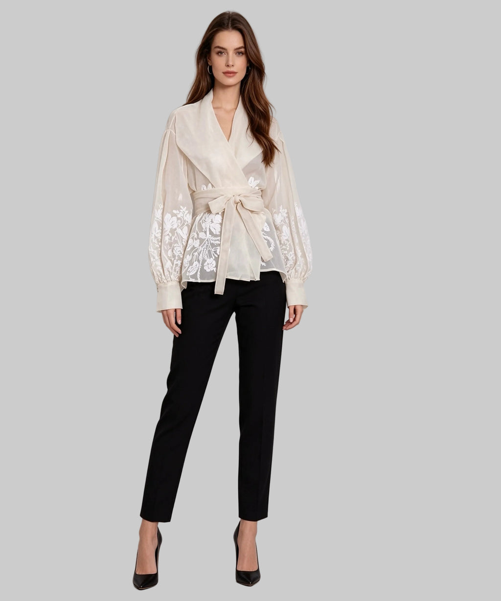 Woman wearing a white lace blouse and black pants on a light gray background