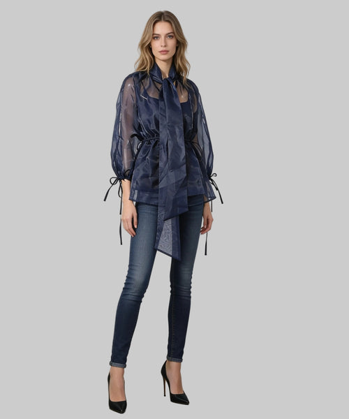 Woman wearing a dark blue sheer blouse with a pattern and high-waisted jeans against a white background.
