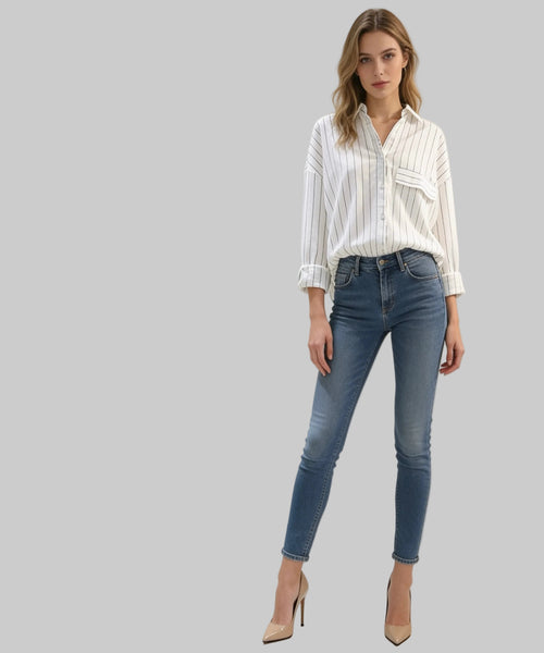 Blonde woman sits on a white background wearing white shirt and jeans