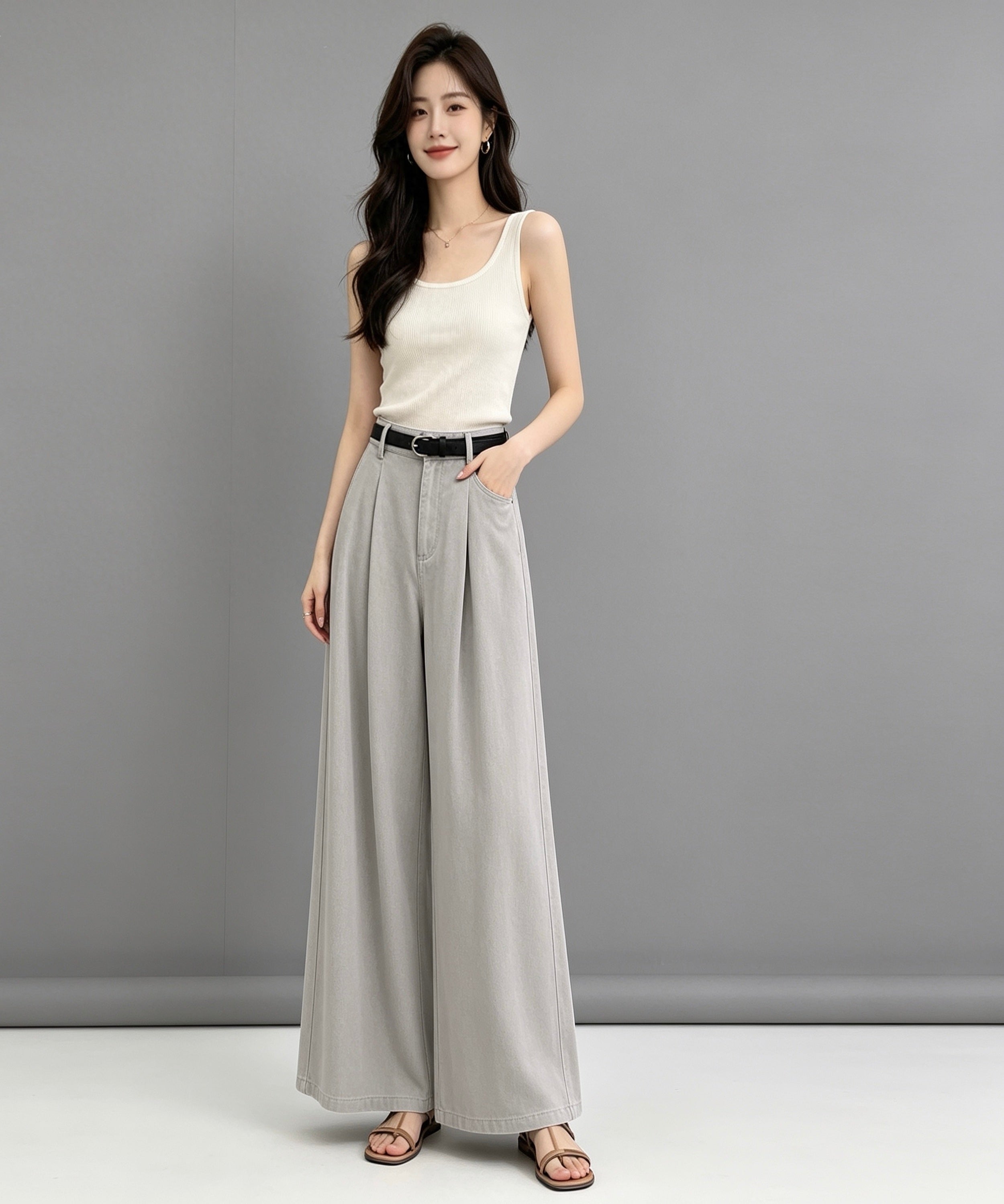 Woman wearing a white sleeveless top and gray wide-leg pants against a gray background