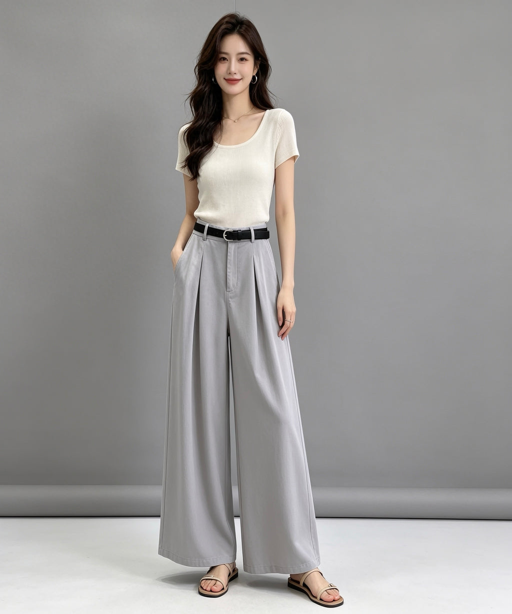 Woman wearing a white top and gray wide-leg pants against a gray background