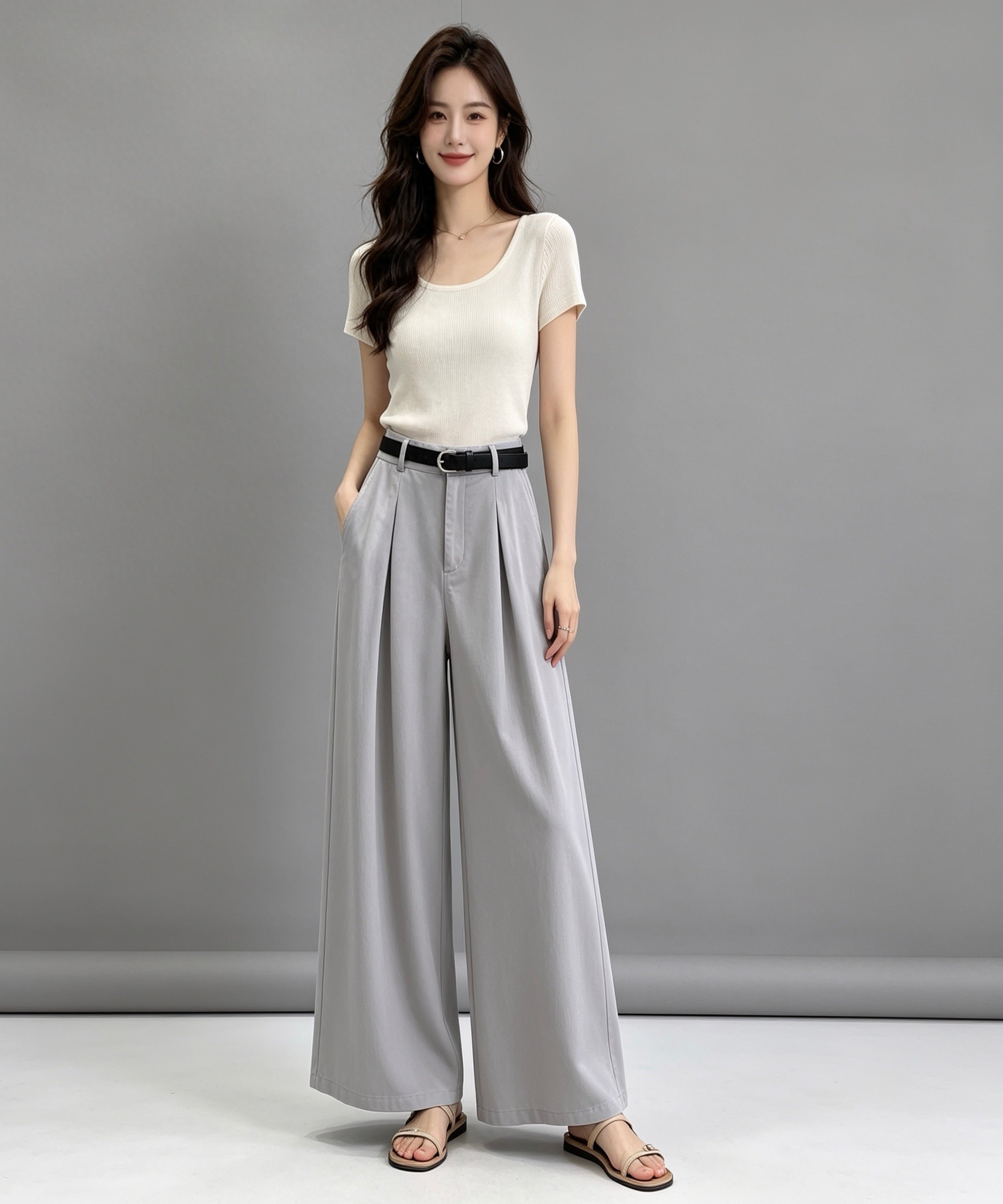 Woman wearing a white top and gray wide-leg pants against a gray background