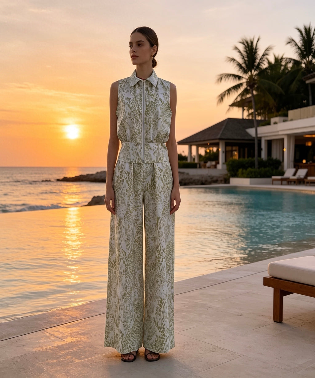 Woman in a patterned outfit standing by a pool with a sunset and palm trees in the background