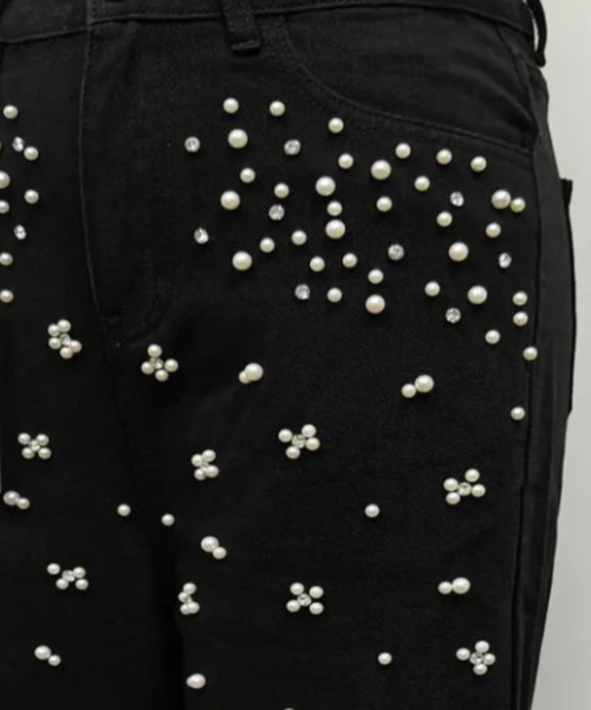 Black pants with pearl embellishments on a plain background