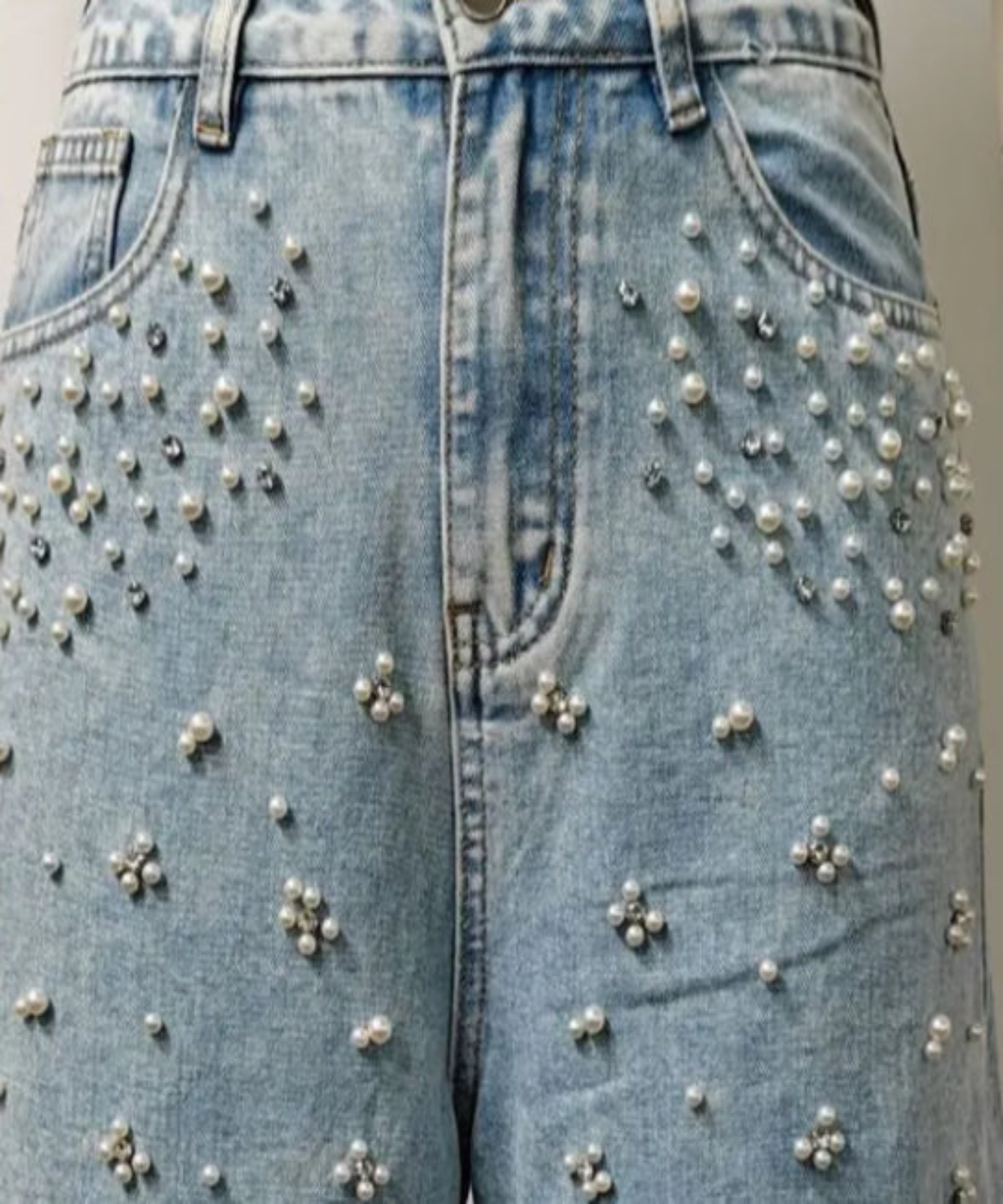 Blue jeans with pearl embellishments on a plain background
