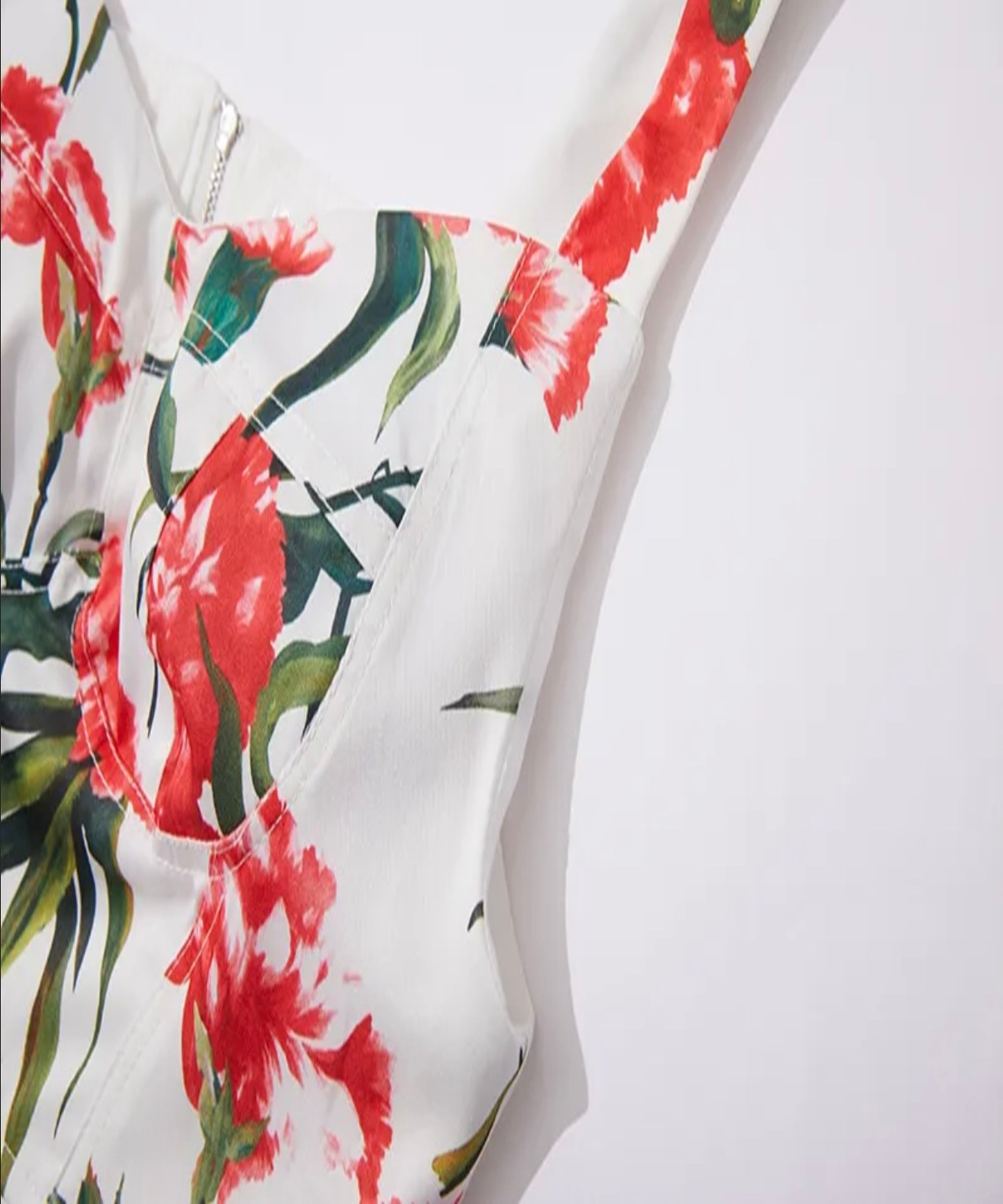 Close-up of a floral-patterned garment with red flowers and green leaves on a white background.