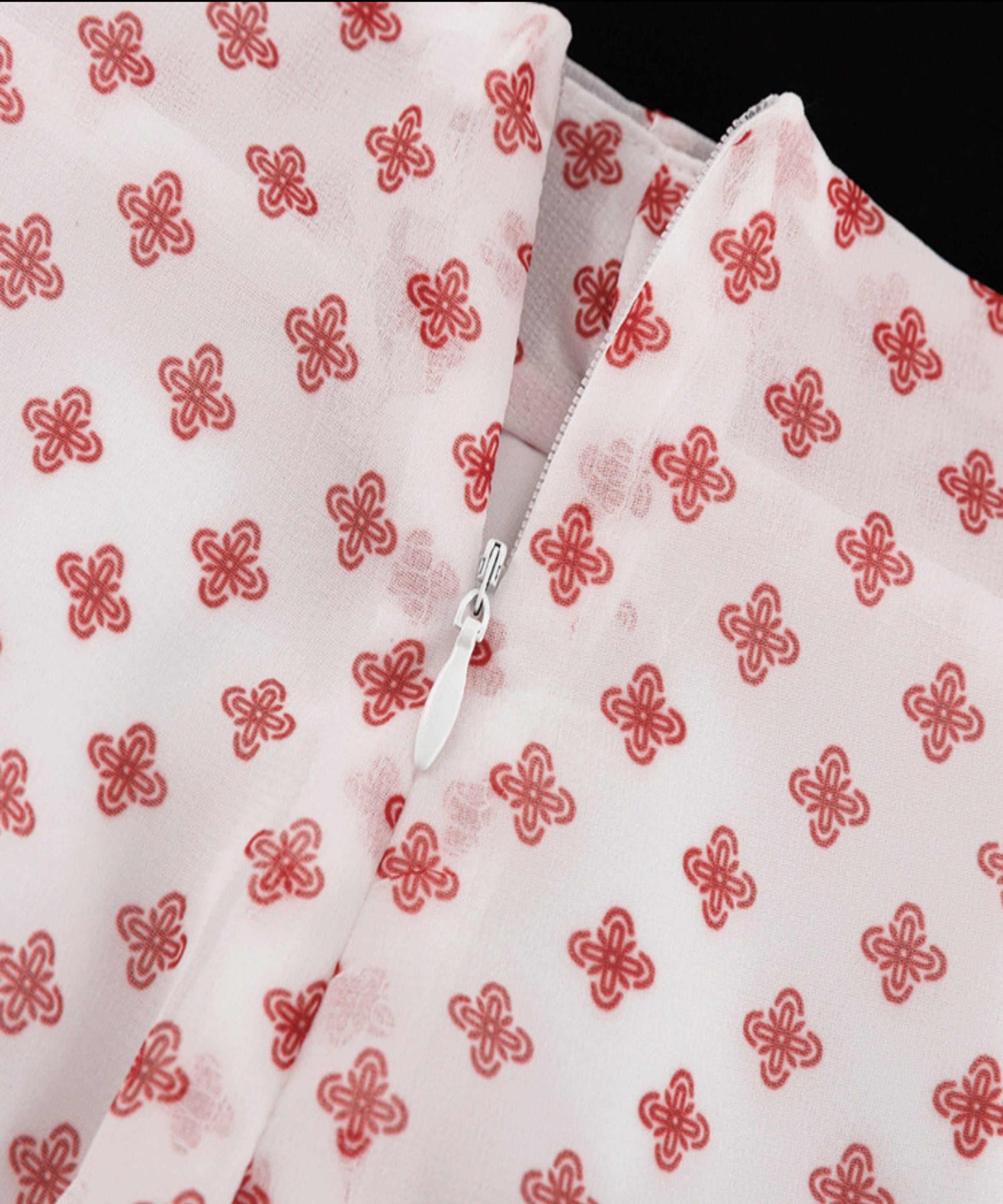 White fabric with red floral patterns and a zipper on a black background