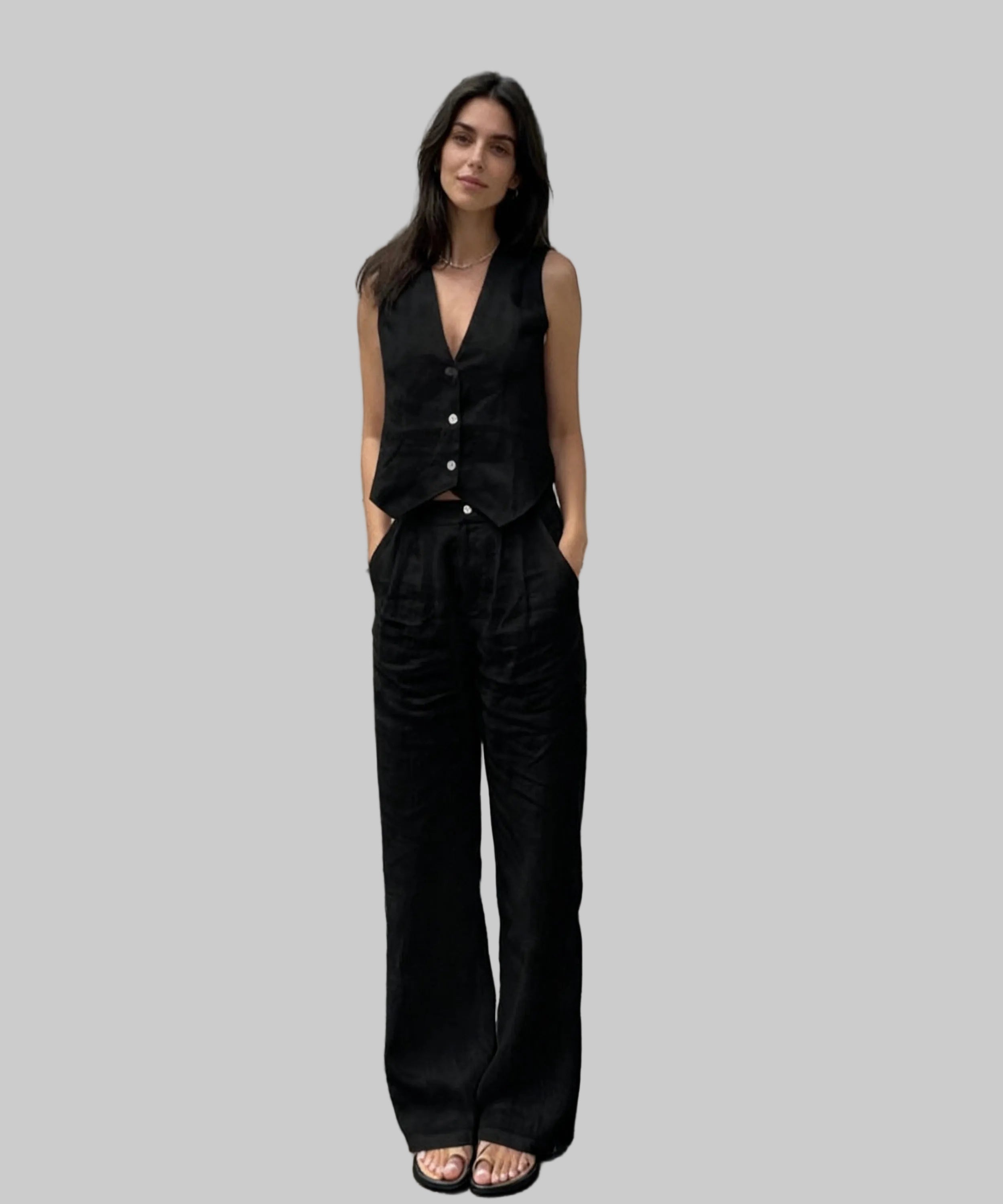 Woman wearing a black sleeveless top and wide-leg pants standing on a white background.