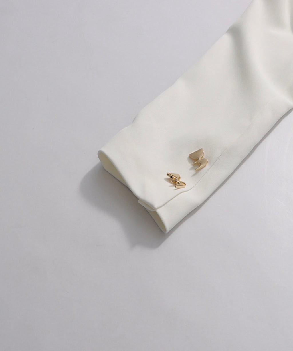 Gold cufflinks on a white shirt cuff against a light gray background