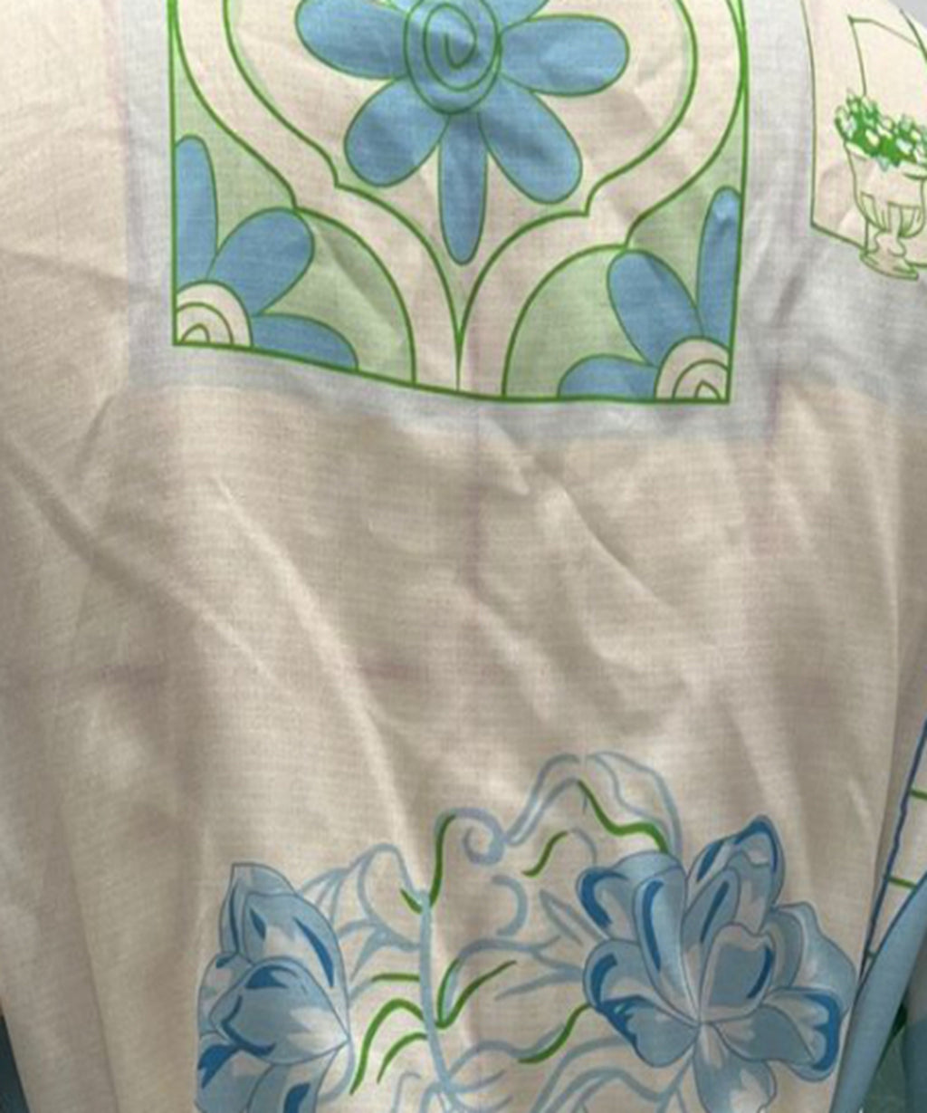 A close-up of a white or off-white fabric with printed floral motifs in light blue and green, showing the texture of the material.