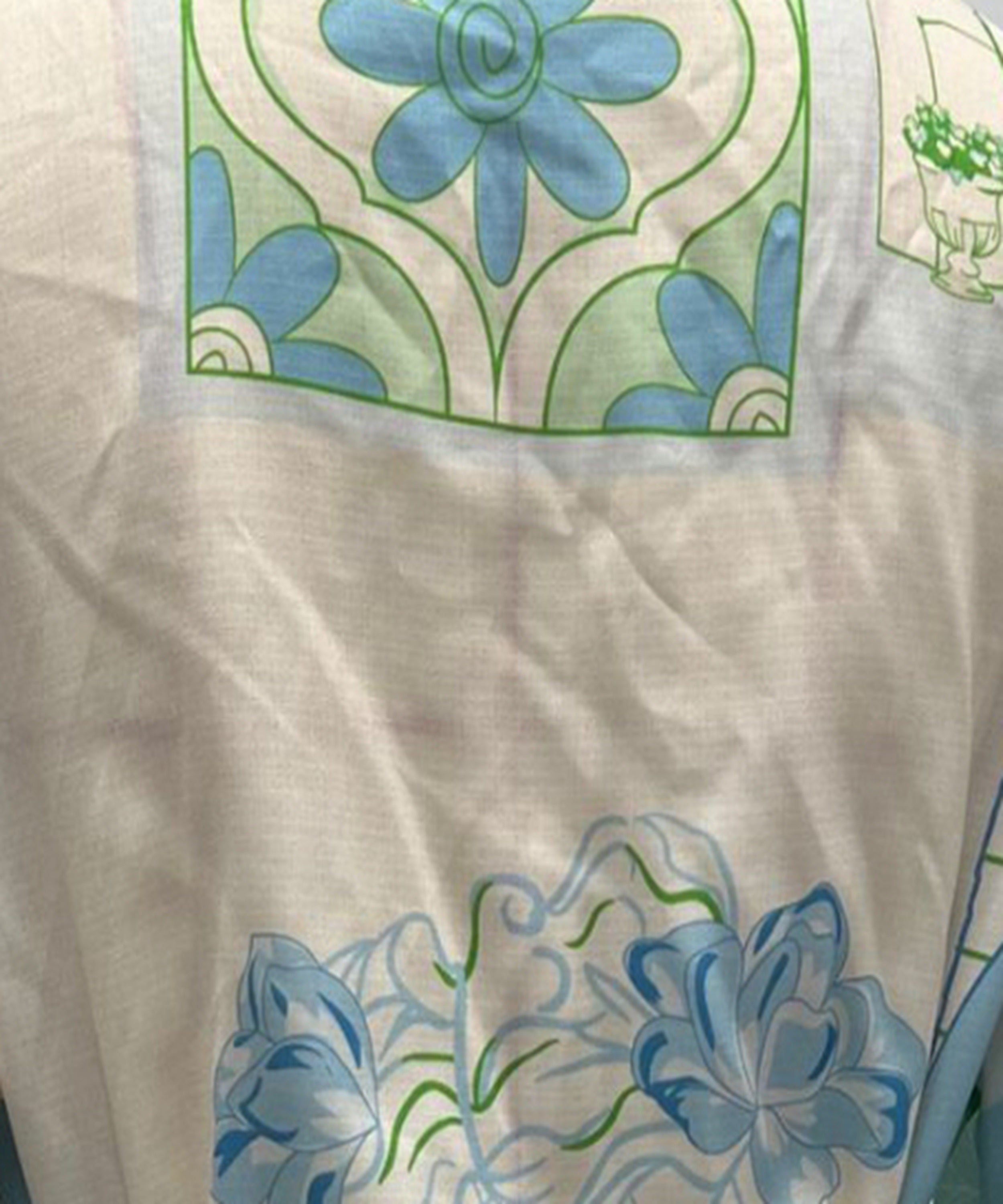 A close-up of a white or off-white fabric with printed floral motifs in light blue and green, showing the texture of the material.