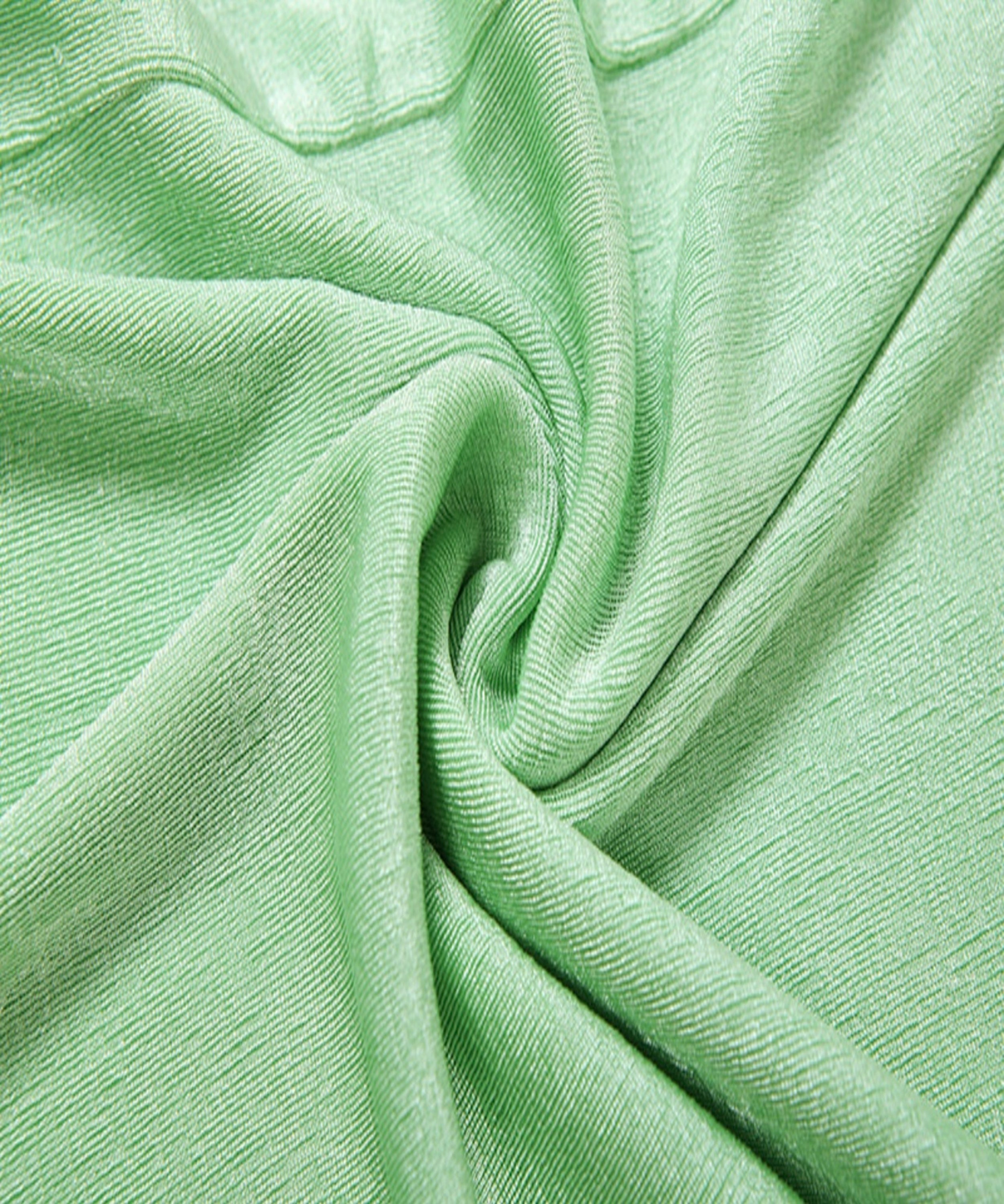 A close-up of light mint green ribbed fabric with soft folds and a twisted swirl pattern.