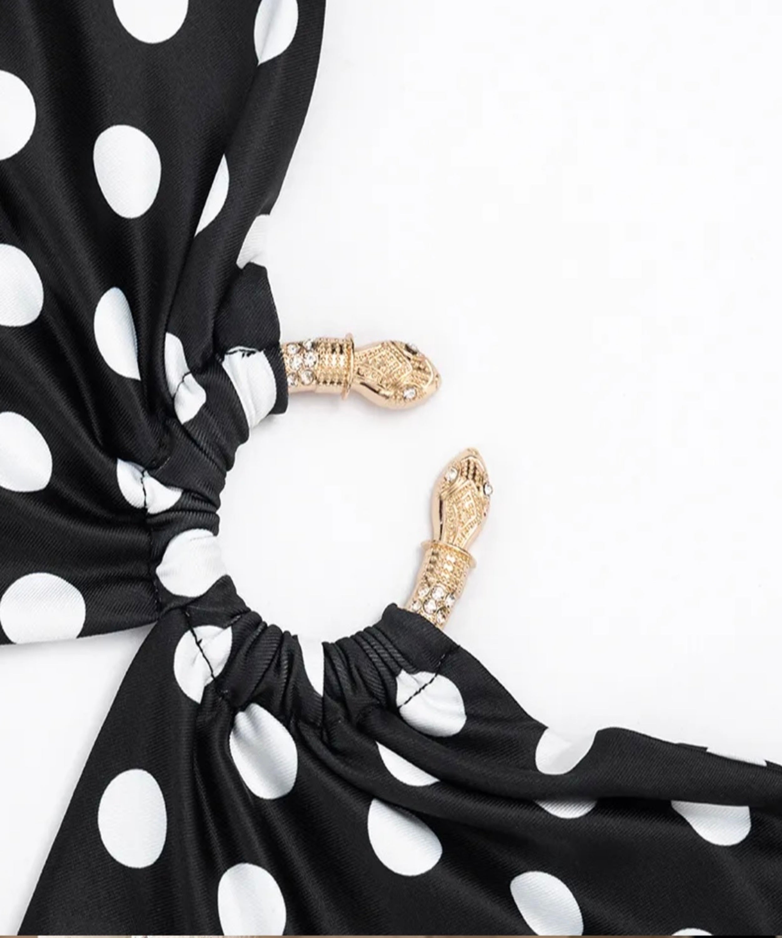 Black and white polka dot fabric accessory with gathered elastic sections and decorative gold-toned hardware, photographed on a plain white background.