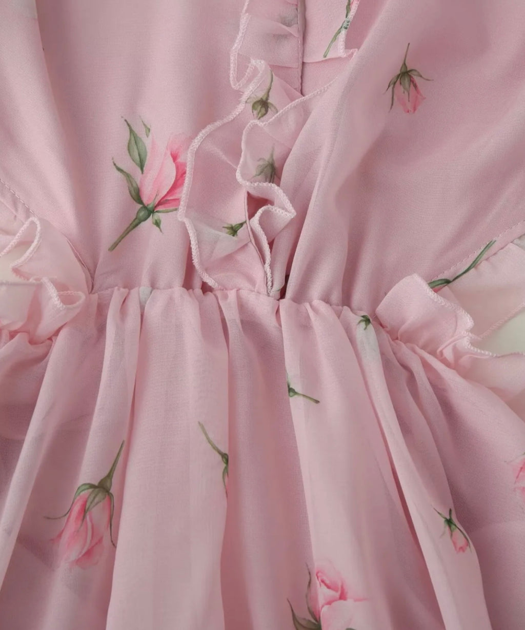 Close-up of a light pink ruffled fabric with a delicate rose and leaf floral print.
