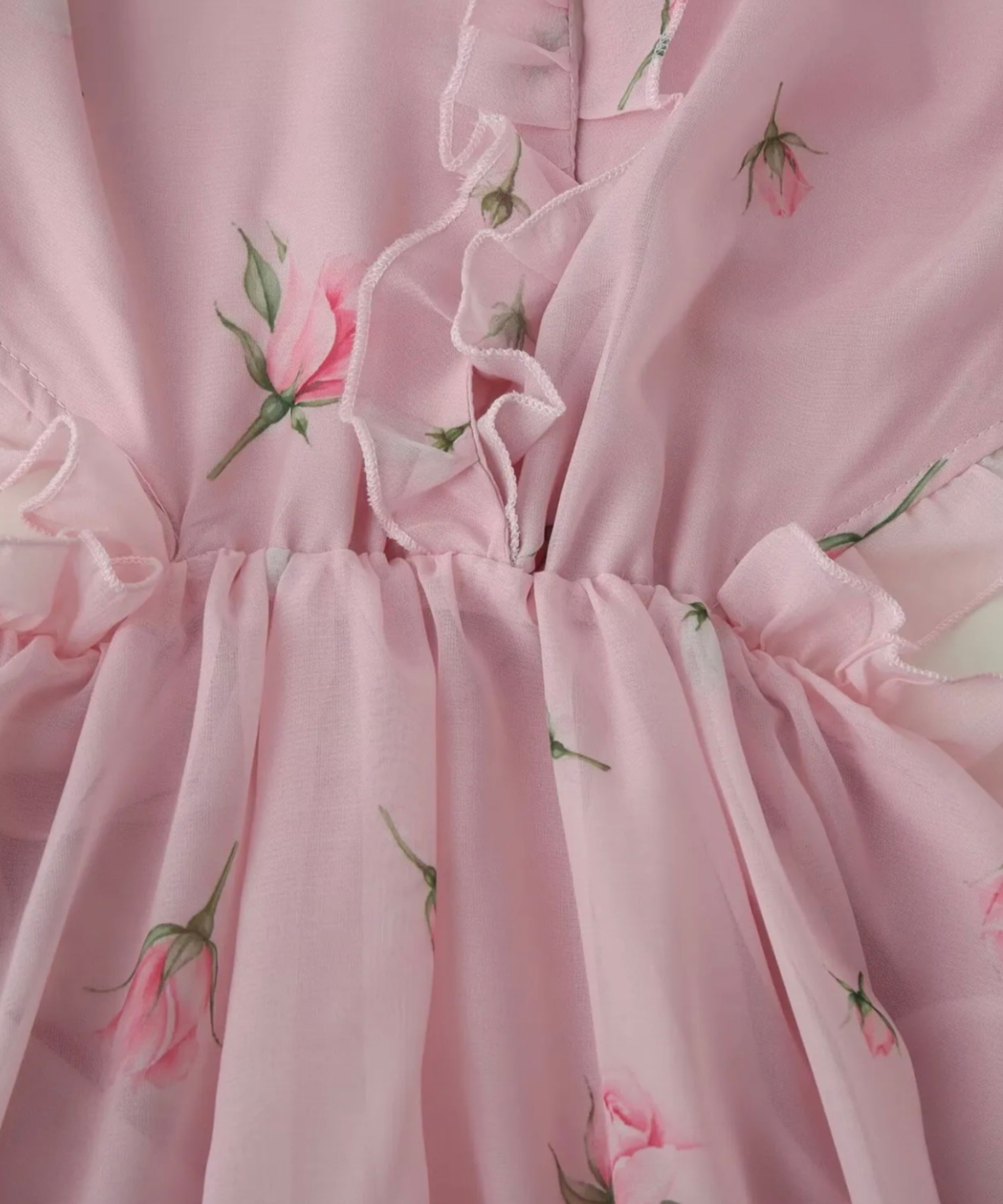 Close-up of a light pink ruffled fabric with a delicate rose and leaf floral print.