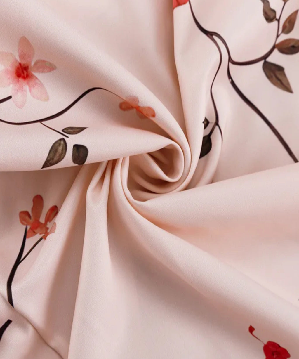 A close-up of draped light blush pink fabric with a delicate floral print featuring dark brown stems, olive green leaves, and soft coral-pink blossoms.